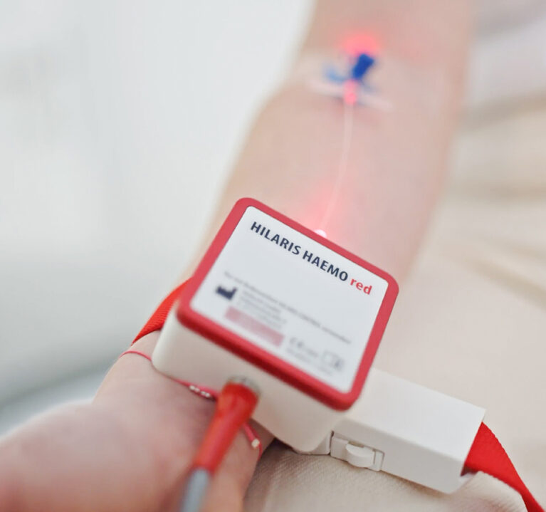 Ein Infusionszugang mit rotem Licht und ein Hämolaser-Apparat mit rotem Licht, aus dem ein Infusionsschlauch führt.