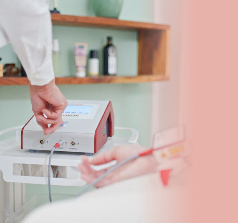 Eine Hand, die den Knopf an einem Apparat drückt. Daneben eine Hand mit Infusionsschlauch.