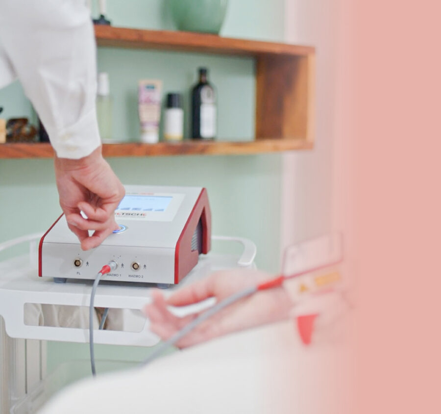 Eine Hand, die den Knopf an einem Apparat drückt. Daneben eine Hand mit Infusionsschlauch.